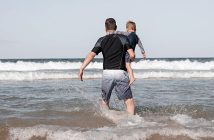 hombre en la playa con un niño en brazos